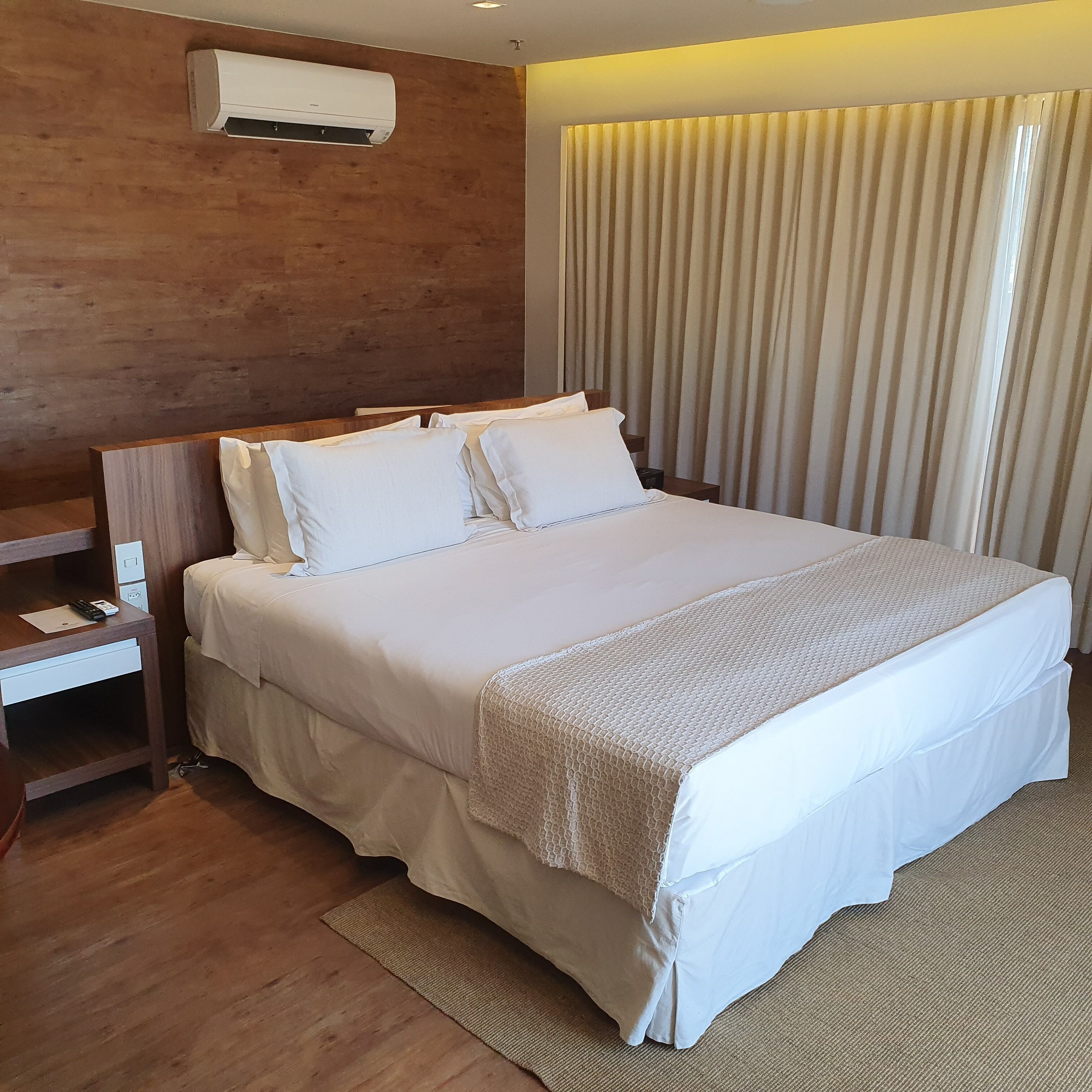 A neatly made bed with white linens, a wooden headboard, and a bedside table with a remote control and a notepad.