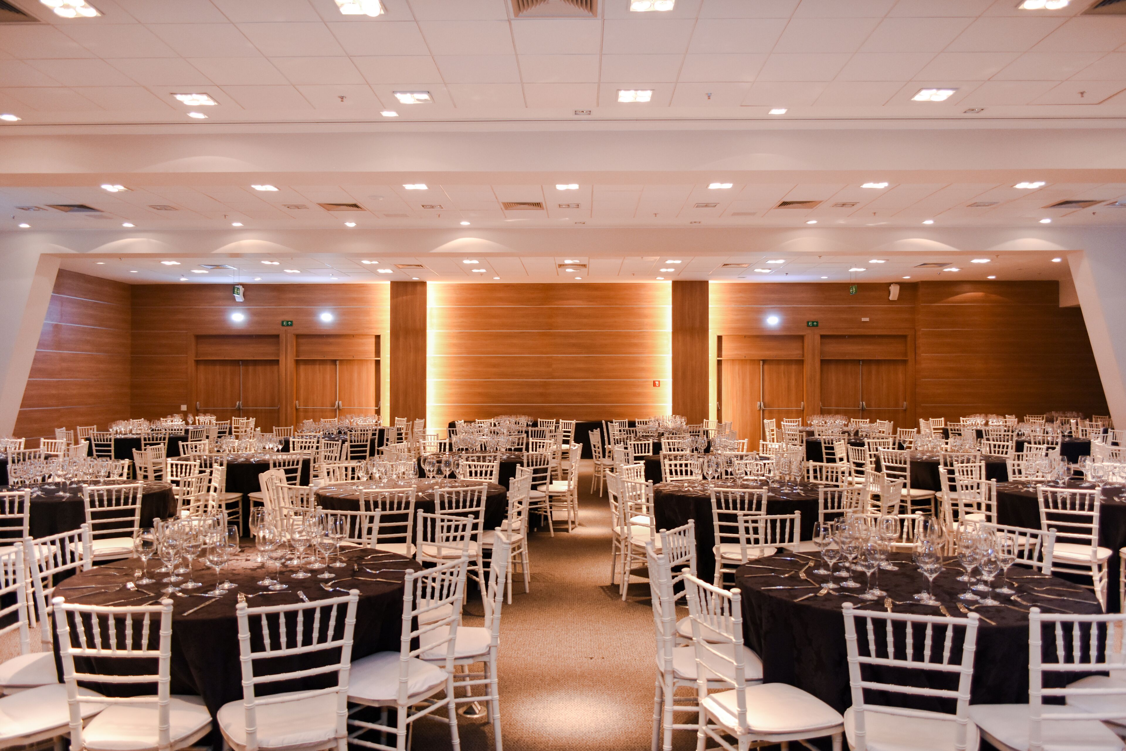 A large banquet hall with multiple round tables, each set with white chairs and black tablecloths.