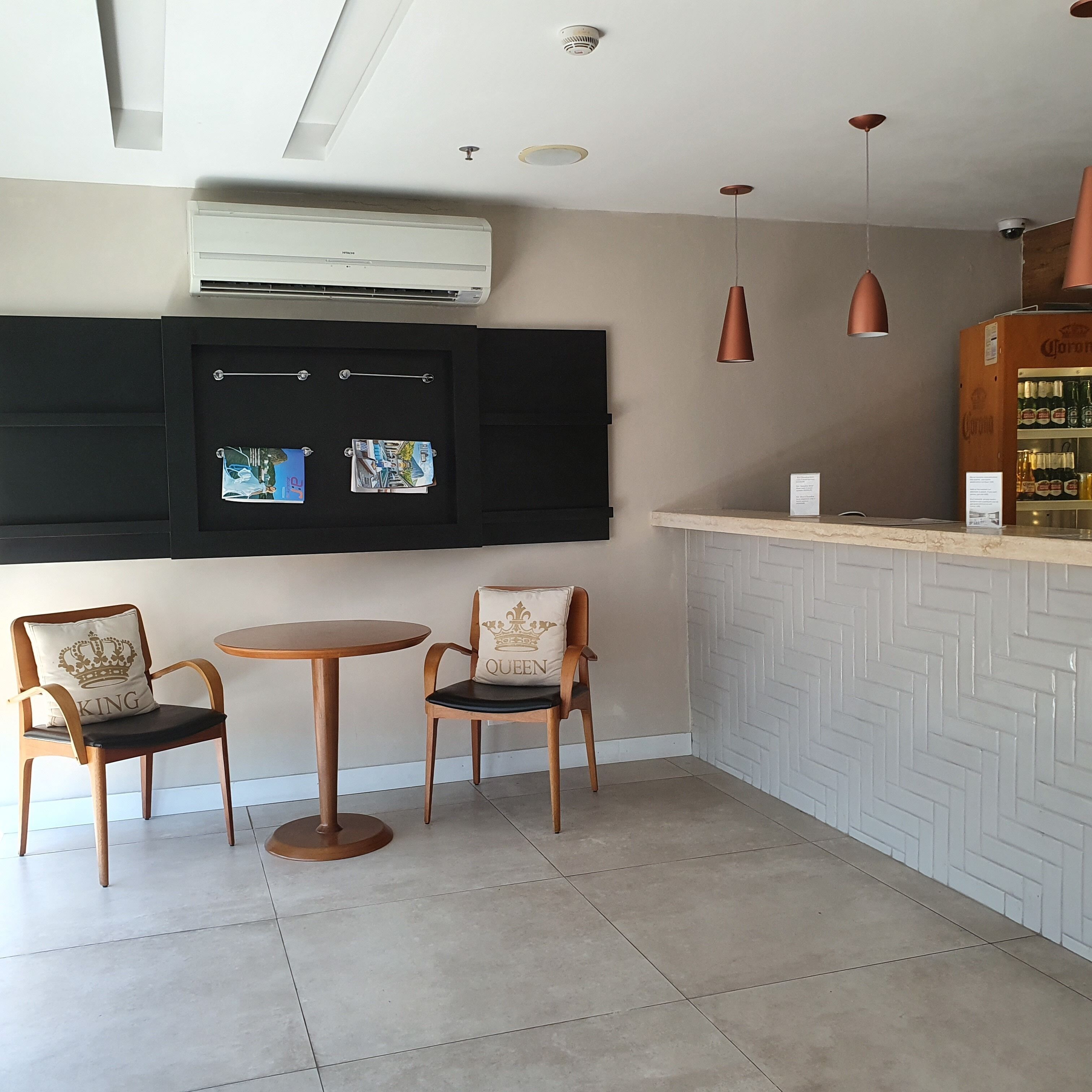 A bar area with two wooden chairs, a round table, a white herringbone-patterned counter, and a Corona beer dispenser.