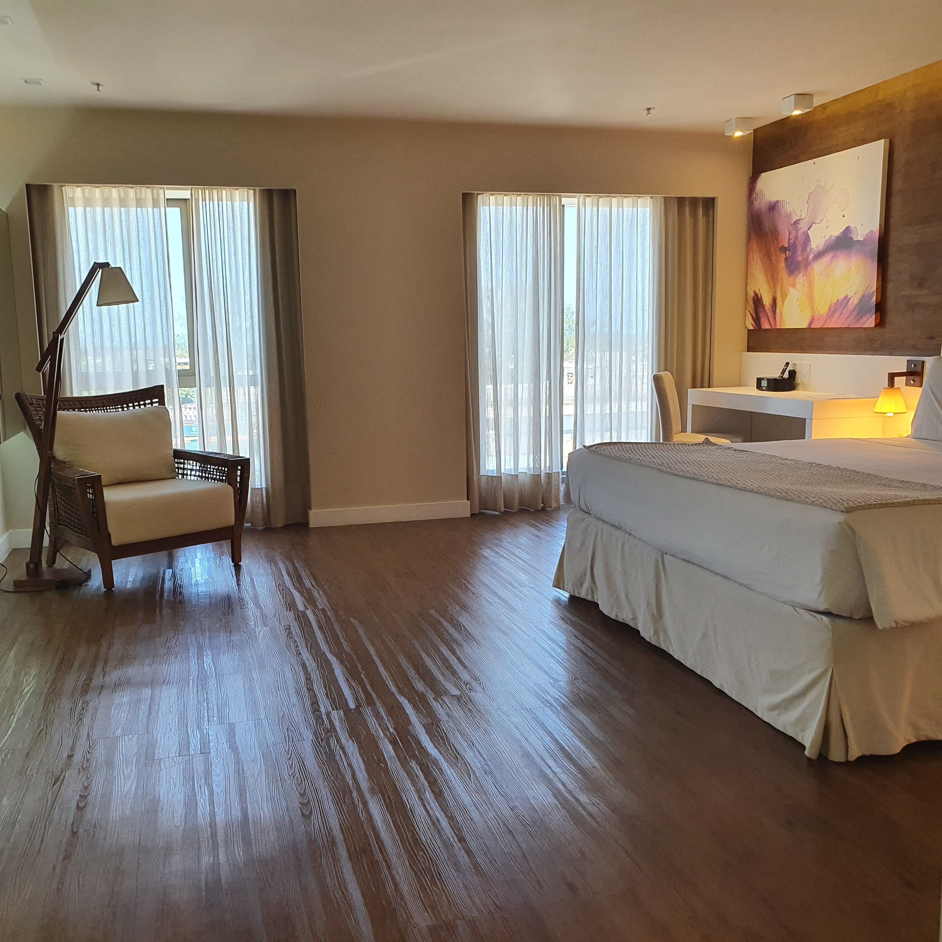 A hotel room with a large bed, a chair, a desk, and a painting on the wall.