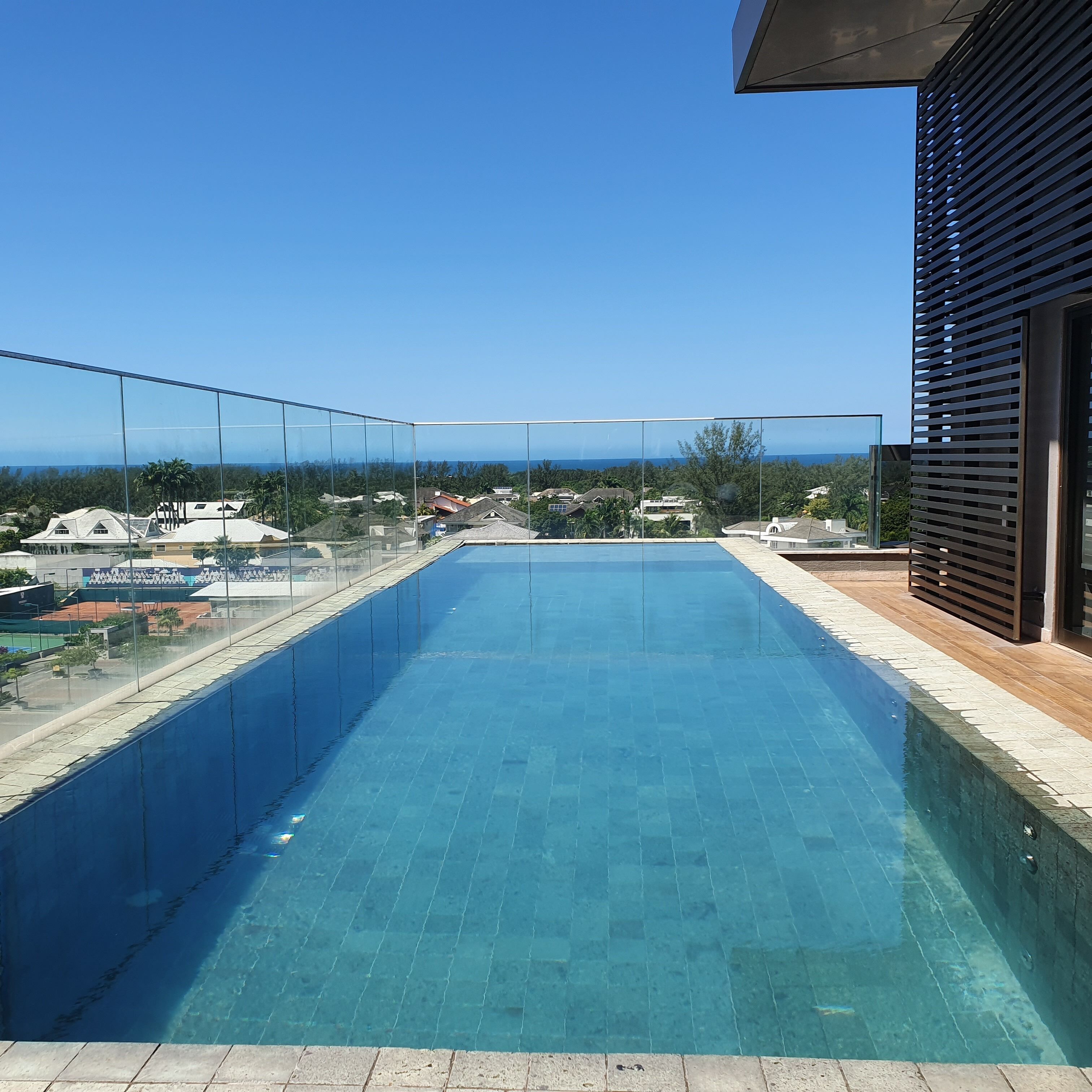 A clear blue pool with a glass barrier, surrounded by a tiled deck and a wooden fence.