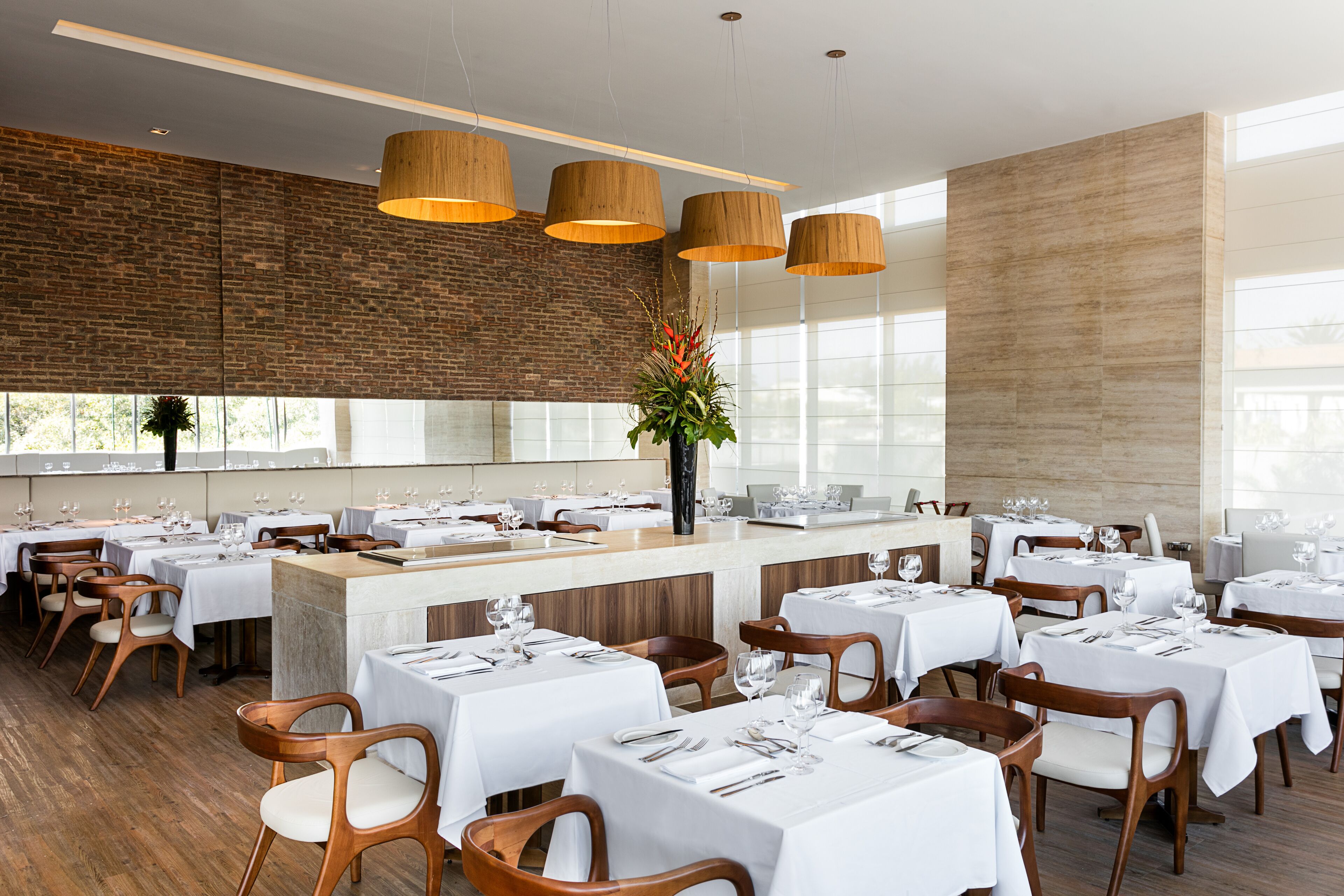 Un restaurante amplio con sillas y mesas de madera, una pared de ladrillo y ventanas grandes.