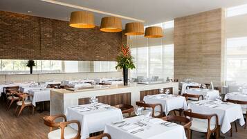 Un restaurante amplio con sillas y mesas de madera, una pared de ladrillo y ventanas grandes.
