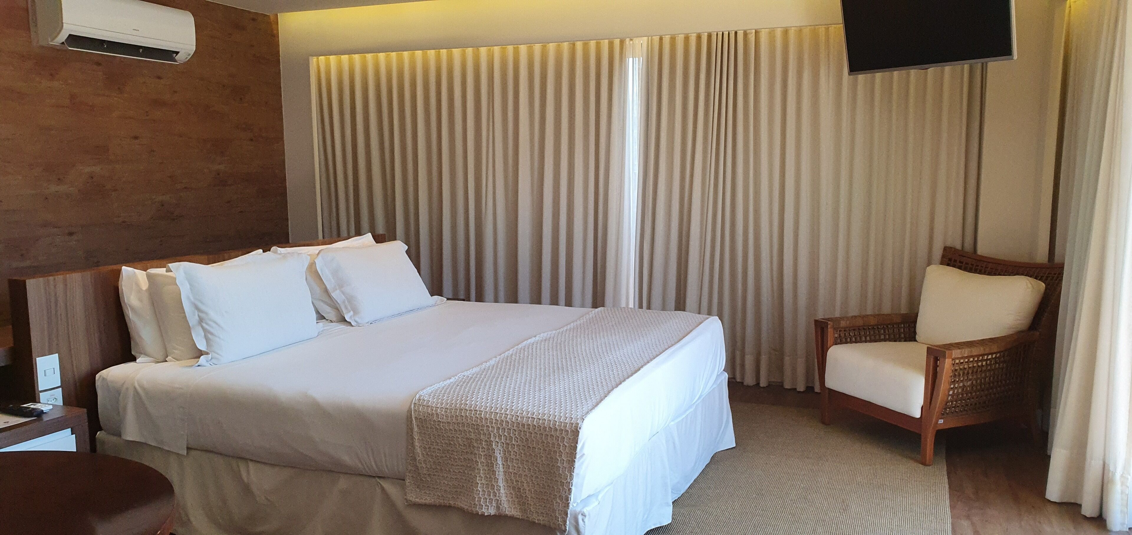 Una habitación de hotel con una cama grande, una silla, un televisor y cortinas.