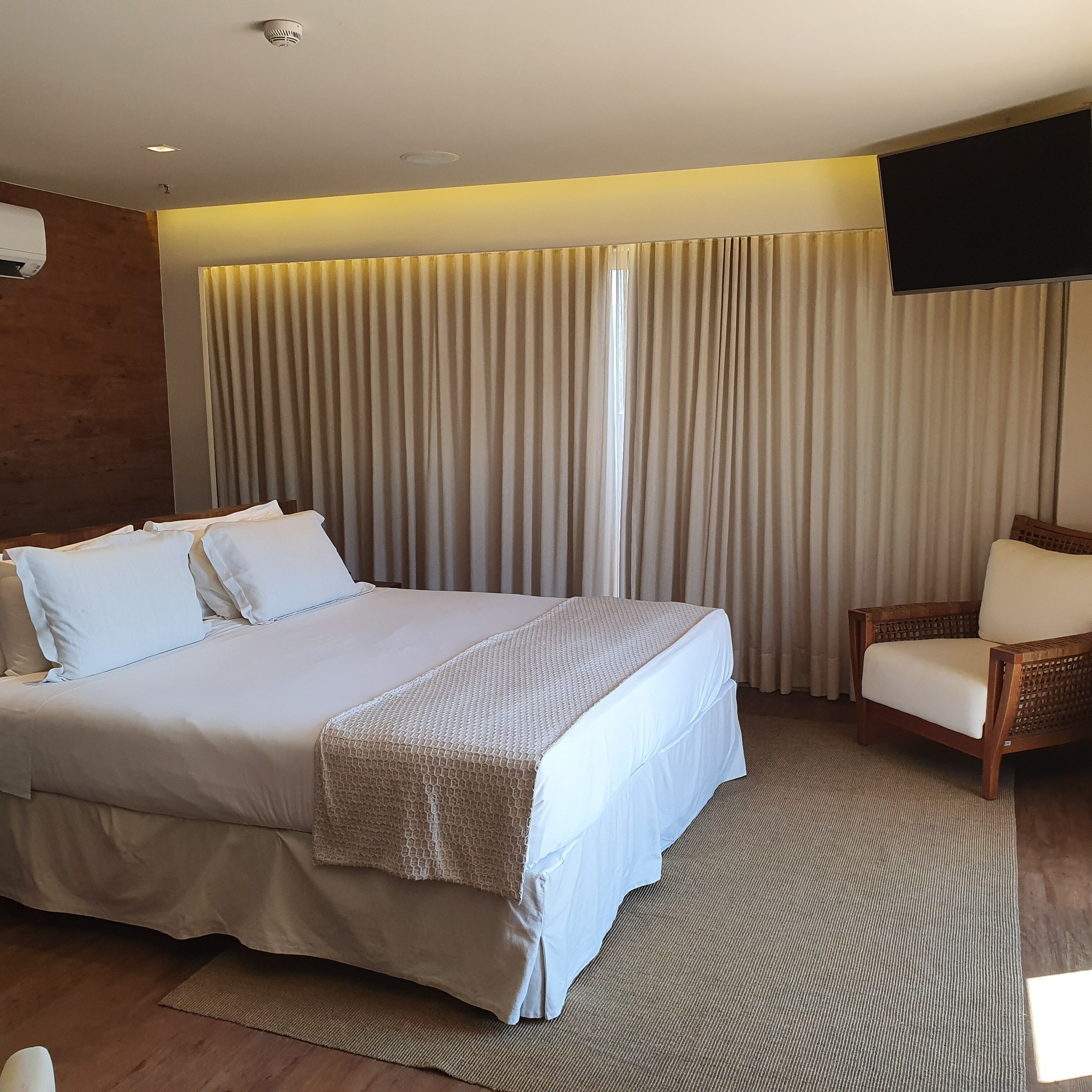 A hotel room with a large bed, a wooden chair, and a TV mounted on the wall.