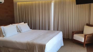 A hotel room with a large bed, a wooden chair, and a TV mounted on the wall.