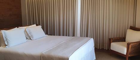 A hotel room with a large bed, a wooden chair, and a TV mounted on the wall.