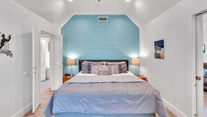 Une chambre avec un grand lit, un ventilateur de plafond et une vue sur le couloir.