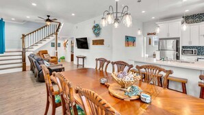 Un vaste espace de salle à manger avec une table et des chaises en bois, une cuisine dotée de meubles blancs et un escalier menant à un autre niveau.