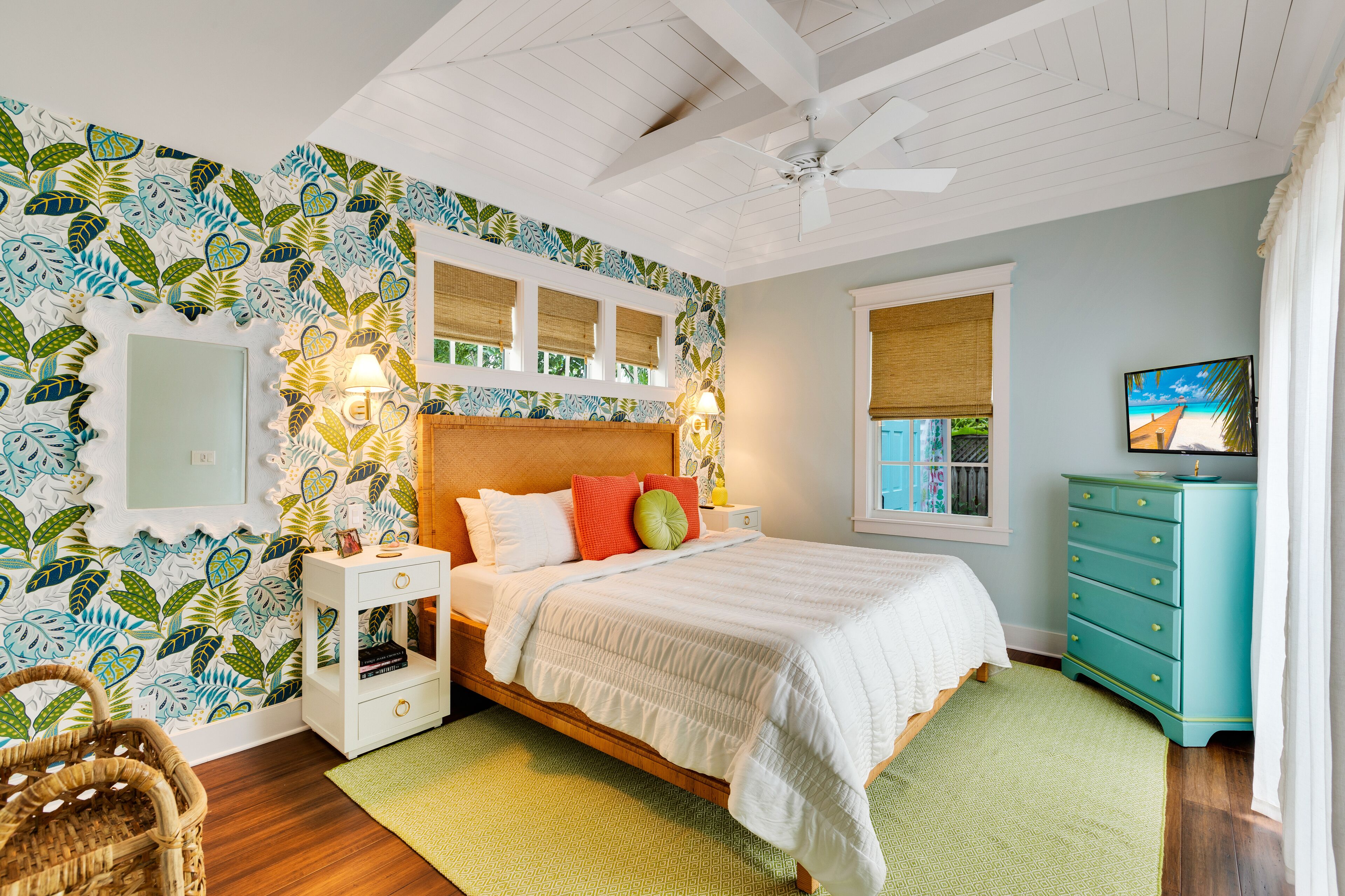 Une chambre à coucher comprenant un lit, des tables de chevet, une commode, une fenêtre et un mur recouvert d’un papier peint à motifs de feuilles.
