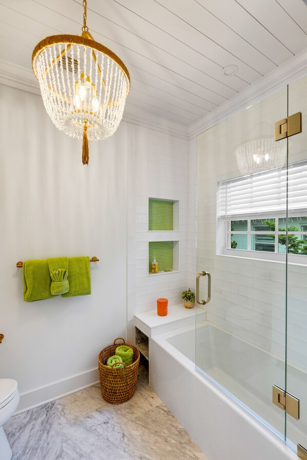 A modern bathroom with a glass-enclosed shower, a freestanding bathtub, and a chandelier.