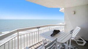 A balcony with a white table and two white chairs, overlooking the ocean.
