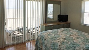 Una camera da letto con un letto, una televisione su una cassettiera e un balcone vista spiaggia.