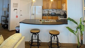 Een moderne keuken met houten kastjes, een zwart aanrecht en twee krukken.