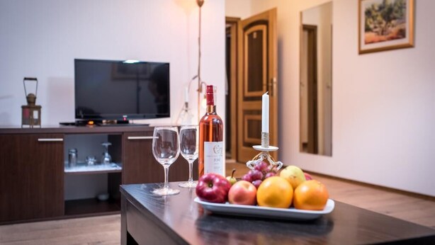 A kitchen area with a dining table set with fruits and wine glasses, a bottle of wine, and a candle.