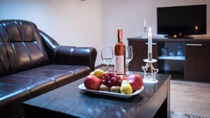 A living room with a dark leather couch, a wooden coffee table with a fruit platter, a wine bottle, two wine glasses, and a candle.