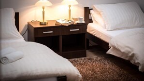 A hotel room with two single beds, a nightstand with lamps, a cup of coffee, and a rolled towel on one bed.