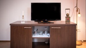 A wooden cabinet with a flat-screen TV on top, a white candle on the left, and a vintage lantern on the right.