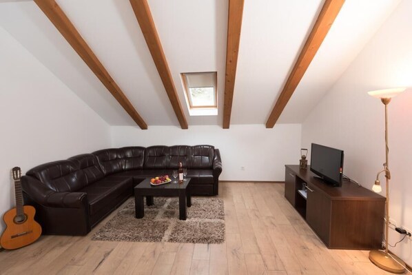 A living room with a dark leather sofa, a wooden coffee table, a small TV on a wooden cabinet, a guitar, and a floor lamp.
