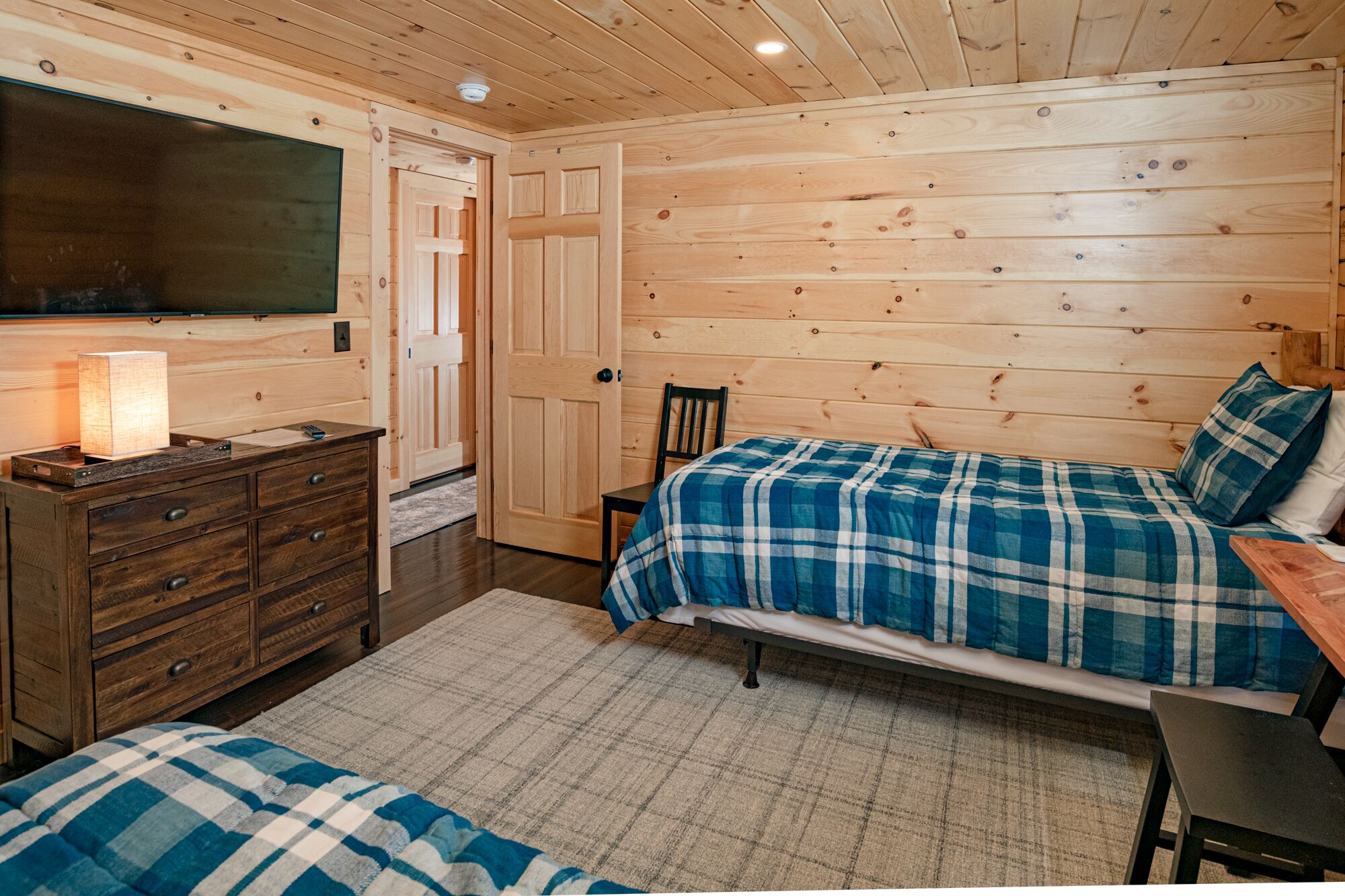A wooden cabin bedroom with a bed, a dresser, a chair, and a television.