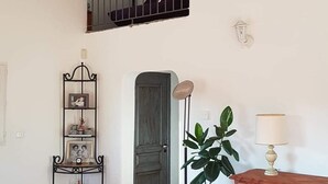Una zona d'estar àmplia amb un sostre alt, una escala de fusta, un balcó amb barana, una planta en test i un moble amb una làmpada.