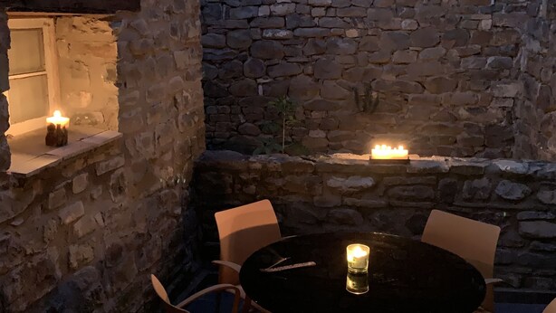 A stone-floored outdoor seating area with a table and chairs, a small window, and a wall-mounted light fixture. - House with a different style for families and groups (Biescas)