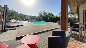Una terraza de madera con piscina, sillas de descanso y una mesa.