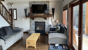 A cozy living room with a stone fireplace, a flat-screen TV, and a wooden bench. - Rocky Mountain Cottage (Nordegg)