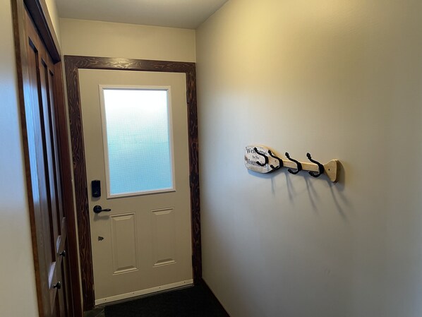 A door with a frosted glass window, a wooden door frame, and a wall-mounted coat rack with hooks. - Rocky Mountain Cottage (Nordegg)