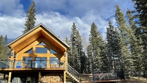 A wooden cabin with a balcony, surrounded by tall pine trees. - Rocky Mountain Cottage (Nordegg)