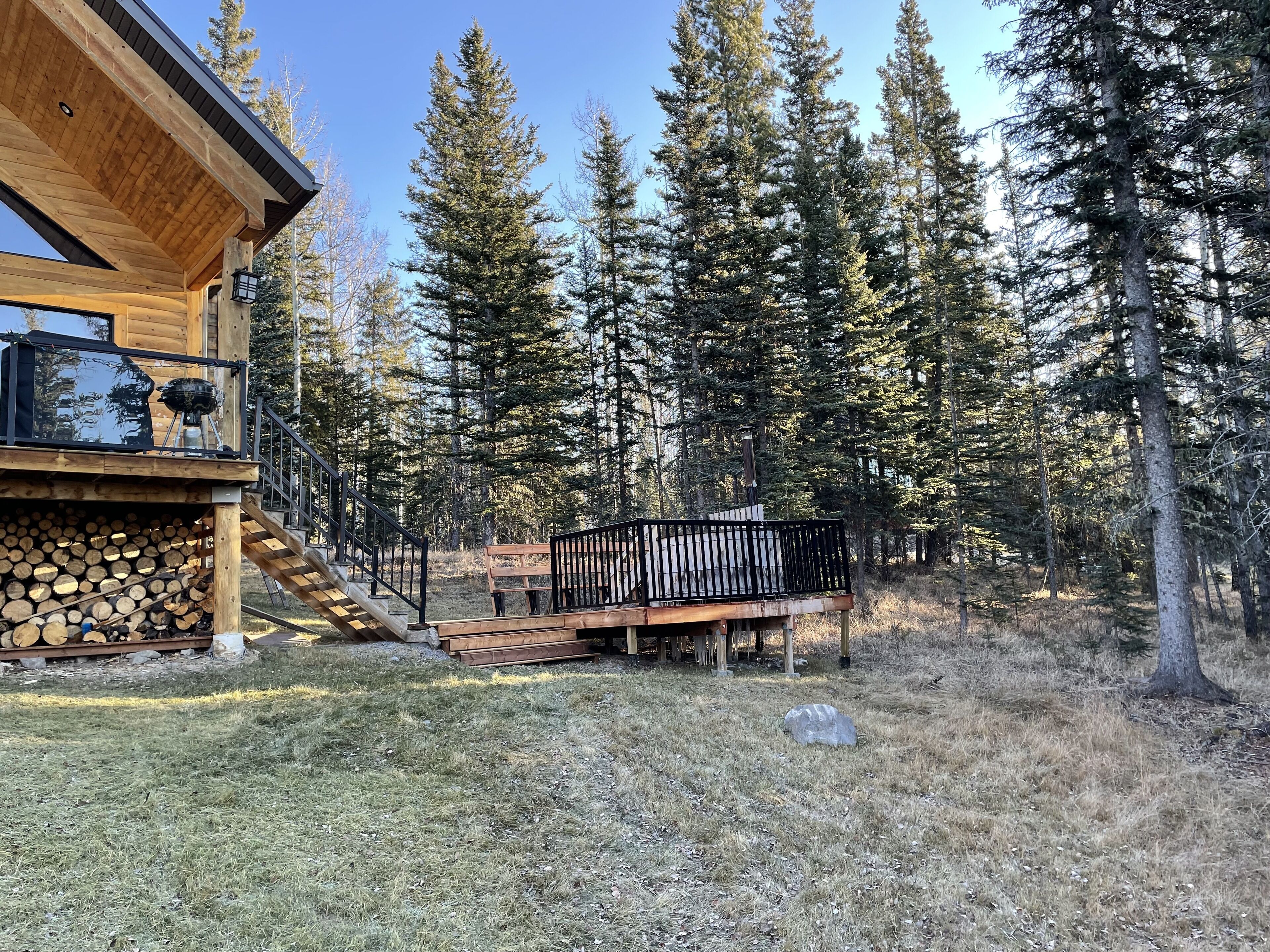 A wooden cabin with a deck, a grill, and a stack of firewood.