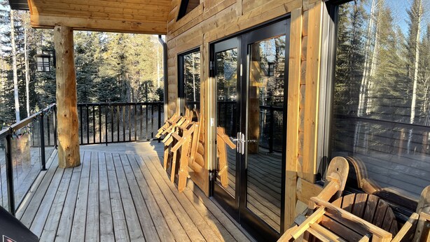 A wooden deck with chairs, a glass door, and a view of trees. - Rocky Mountain Cottage (Nordegg)