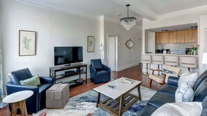 Una sala de estar con televisor, dos sofás, una mesa de centro y un área de cocina con taburetes de bar.
