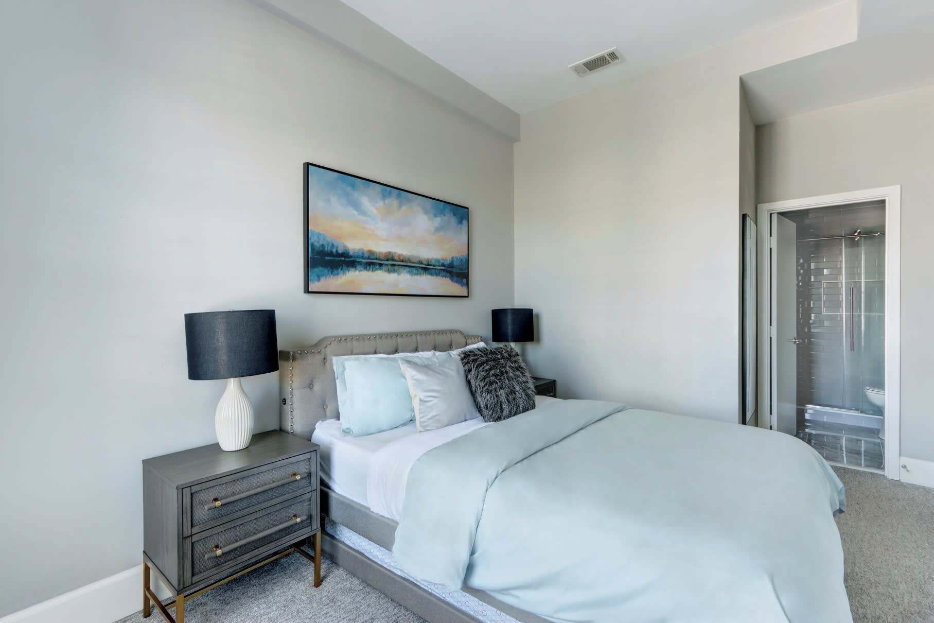 A bedroom with a bed, nightstands, a painting, and a shower area.