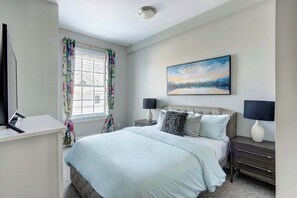 Une chambre à coucher avec un lit, deux tables de chevet, une télévision et une fenêtre avec des rideaux.