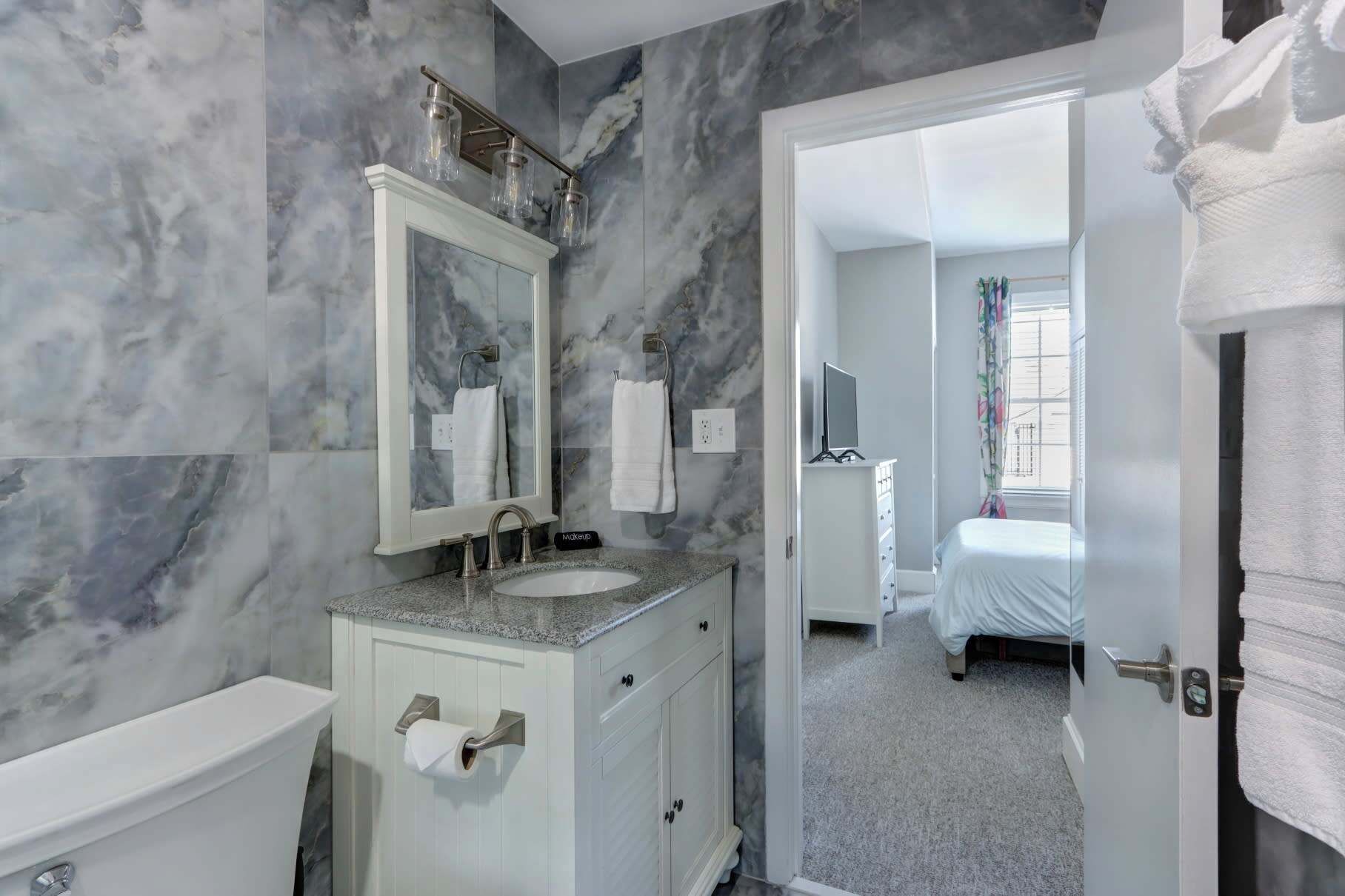 Un baño con pared de mármol, un lavabo, un espejo y un inodoro.