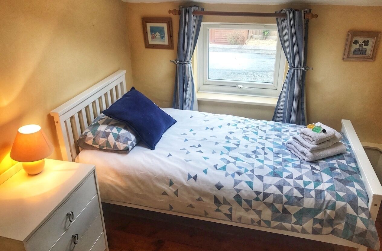 Een net opgemaakt bed met een geometrisch beddegoed, een blauw kussen en een stapeling opgevouwen handdoeken aan de zijkant.
