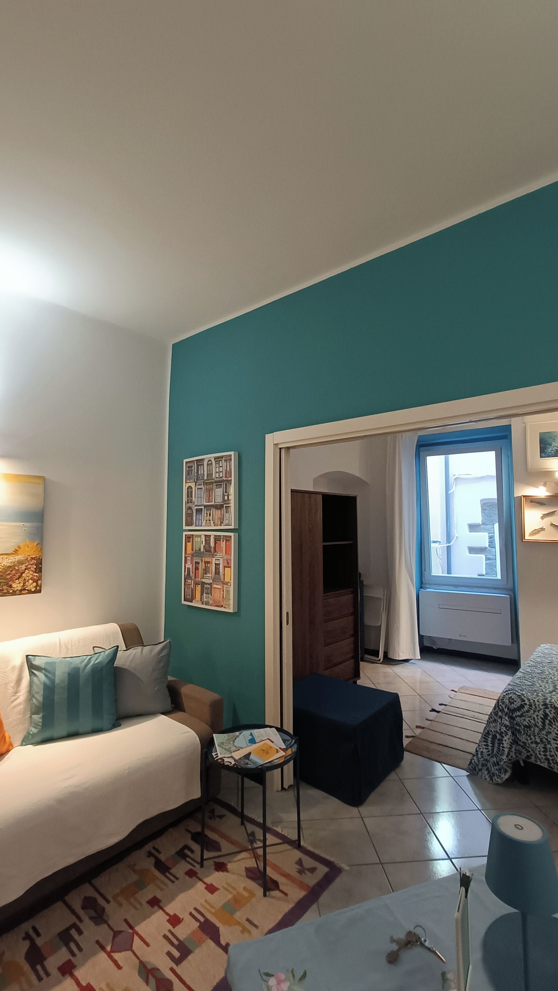 Un salon avec un mur d’accent de couleur turquoise, un canapé blanc, une petite table ronde et un tapis à motifs.