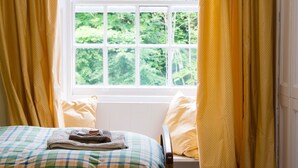 Une chambre avec un lit, une fenêtre avec des rideaux et une vue sur la verdure à l’extérieur.