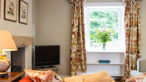 Une chambre avec un lit, une télévision, une lampe, une fenêtre avec des rideaux et des tableaux encadrés accrochés au mur.