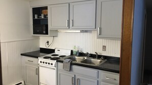 Una cocina compacta con gabinetes blancos, una encimera negra, una estufa y un lavamanos.