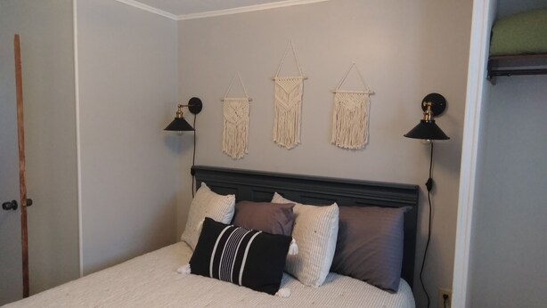 Un dormitorio con cama, dos lámparas de pared y tres tapices de macramé.