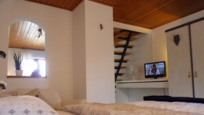 A bedroom with a bed, a desk with a computer, a window with a plant, and a wooden ceiling. - HOUSE TOURNEUR - Beautiful apartment with fireplace (Lippetal)