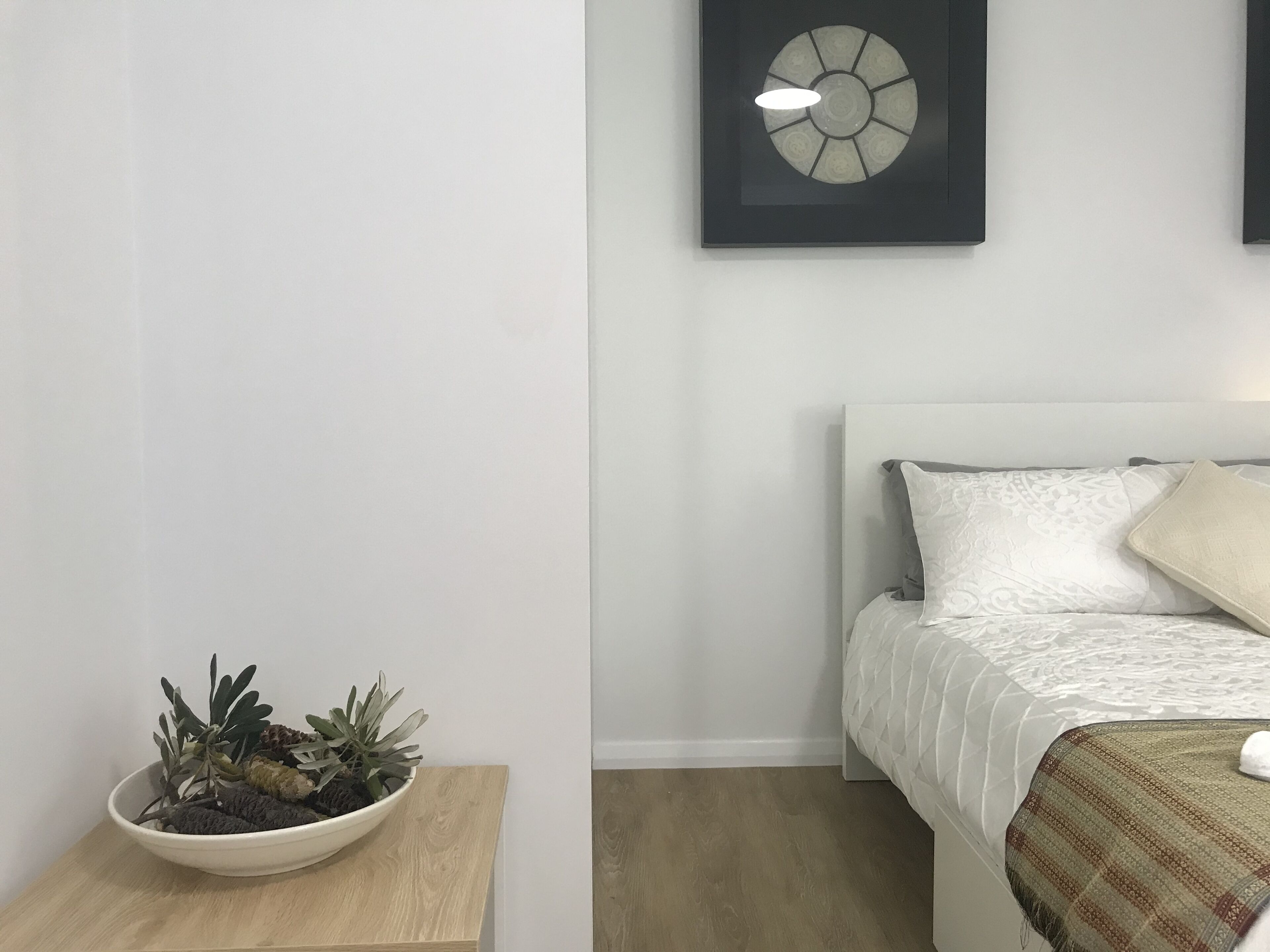 Et soveværelse med seng, et natbord med plante, og en vægmonteret lampe.
