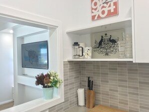 Een moderne keuken met een raam, een wandgemonteerde televisie, een decoratieve wandversiering en een plank met keukengerei.
