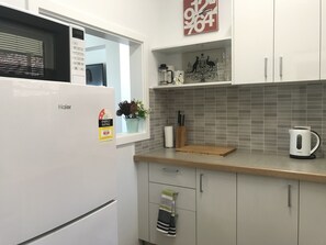 Een keuken met een witte koelkast, een grijze betegelde achterwand en een houten aanrecht.