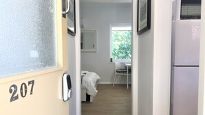 A hallway leading to a bedroom with a bed, a desk, and a window.