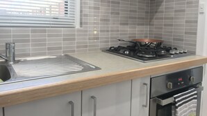 A kitchen with grey tiles, a gas stove, a sink, and a window with blinds.