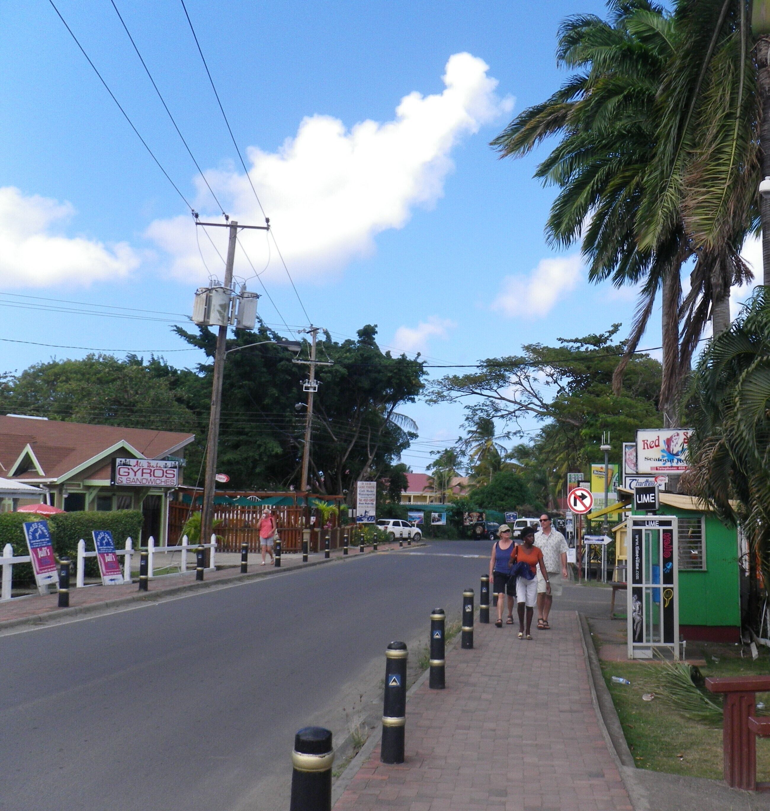 A street with a sidewalk, a building with a sign for 'GYROS & SANDWICHES', and a 'LIME' sign.