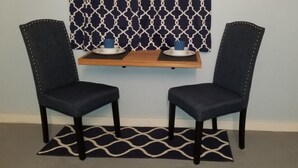 Two dark blue upholstered chairs with metal studs, a wooden shelf with two white plates and blue cups, and a black and white patterned rug on a light blue wall with a geometric patterned curtain. - Careffe Suites - Studio unit 4 - 5 mins drive to Rodney Bay Village (Monchy)